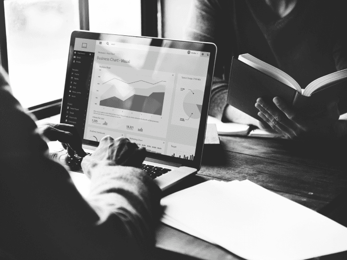 Uma pessoa segurando um livro nas mãos e outra pessoa com as mãos sobre o notebook